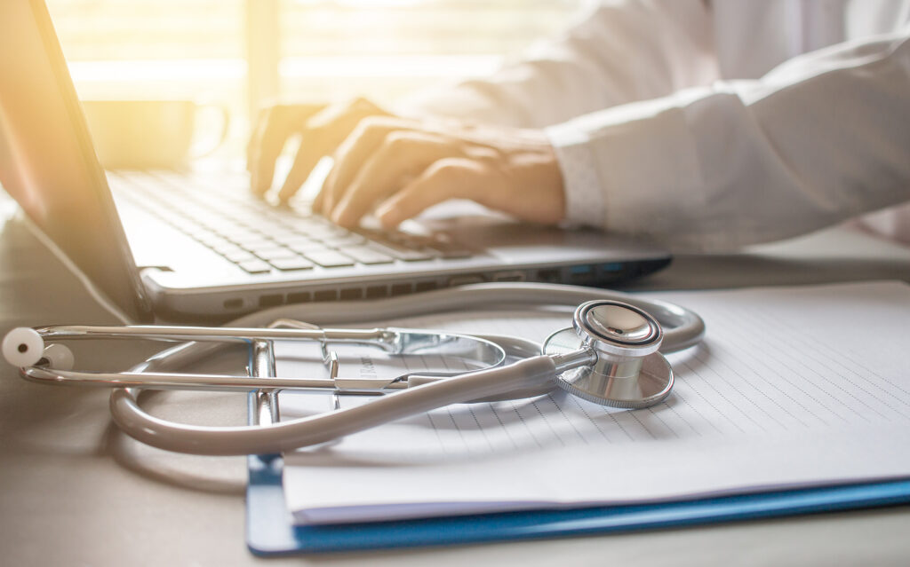 Stethoscope on prescription clipboard and Doctor working an Laptop on desk